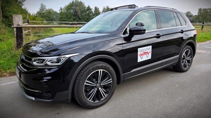 Schwarzer SUV mit Aufkleber, parkt auf einer Straße neben Bäumen.